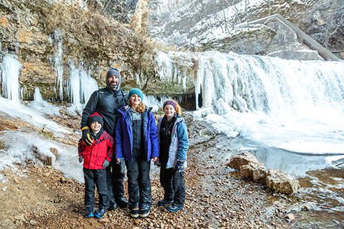 A family outside in the winter by a frozen waterfall.