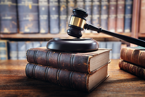 A short stack of law books with a judge's gavel on top and shelves of more books in background