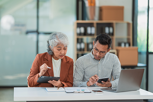 Two people work together at a table to prepare tax documents.