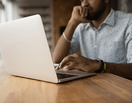 Man typing on laptop and cupping chin in thought