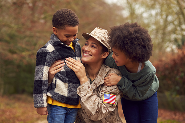 A mother in military uniform hugging two children.