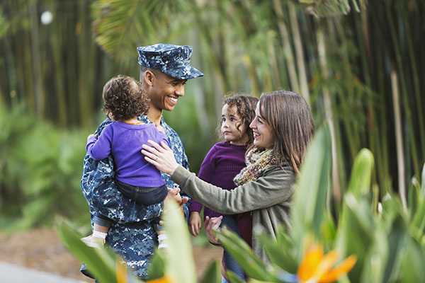A man in military fatigues embracing a woman and two children on a wooded walking path