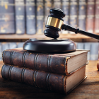 A short stack of law books with a judge's gavel on top and shelves of more books in background
